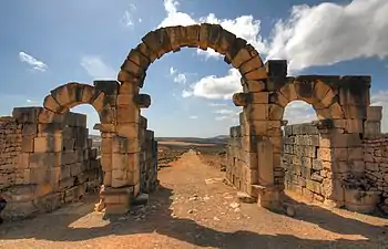 View through a triple-arched gate looking downhill to a street lined with ruins