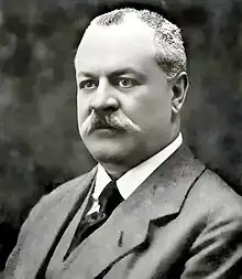 A middle-aged, mustached caucasian man, wearing a business suit