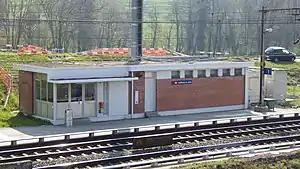 Boxy single-story building on platform next to double-tracked railway line