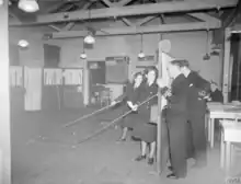 A wargame in progress. The men on the far-right command the escort ships and may only view the game board through holes in the screen. The woman in the foreground is Jean Laidlaw.