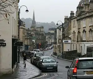 Street scene with shops and houses. Church tower in the distance.