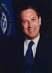 A color portrait of a man in his forties wearing a suit and standing beside a handrail