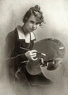 formal, hip height portrait of young woman with long hair pulled up into a knot, wearing long sleeved dark velvet dress with light collar, holding a paintbrush and palette