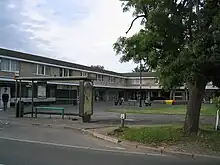 Row of shops in pedestrianised precinct. In the foreground a bus shelter and tree.