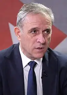 A photograph of Zdravko Ponoš in a blue suit while being interviewed by Južne vesti