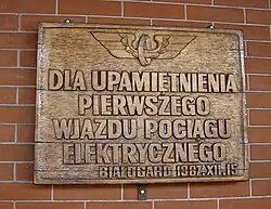 Tablica pamiątkowa na murze budynku dworca upamiętniająca elektryfikację kolei