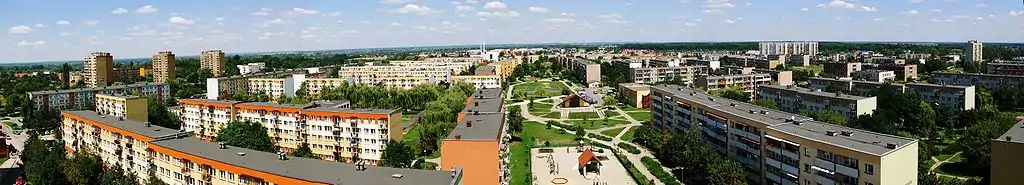 Panorama Serbinowa. Po lewej stronie wieżowce Osiedla Centrum (nazywanego tarnobrzeskim Manhattanem). W oddali park i Zamek Dzikowski. W środku zdjęcia skwer między blokami, bez oficjalnej nazwy, nazywany przez mieszkańców Pigal (Pigalle). Centralnym punktem skweru jest mały amfiteatr z charakterystycznym trójkątnym dachem (obecnie głównie pijalnia piwa). Za nim kościół. Na horyzoncie dostrzec można Sandomierz. Na prawo od skweru – dawna Biblioteka, obecnie Tarnobrzeska Agencja Rozwoju Regionalnego. Po prawej stronie widoczne również wieżowce Bogdanówki, las Zwierzyniec oraz Szkoła Podstawowa Nr 10 i jej boisko.