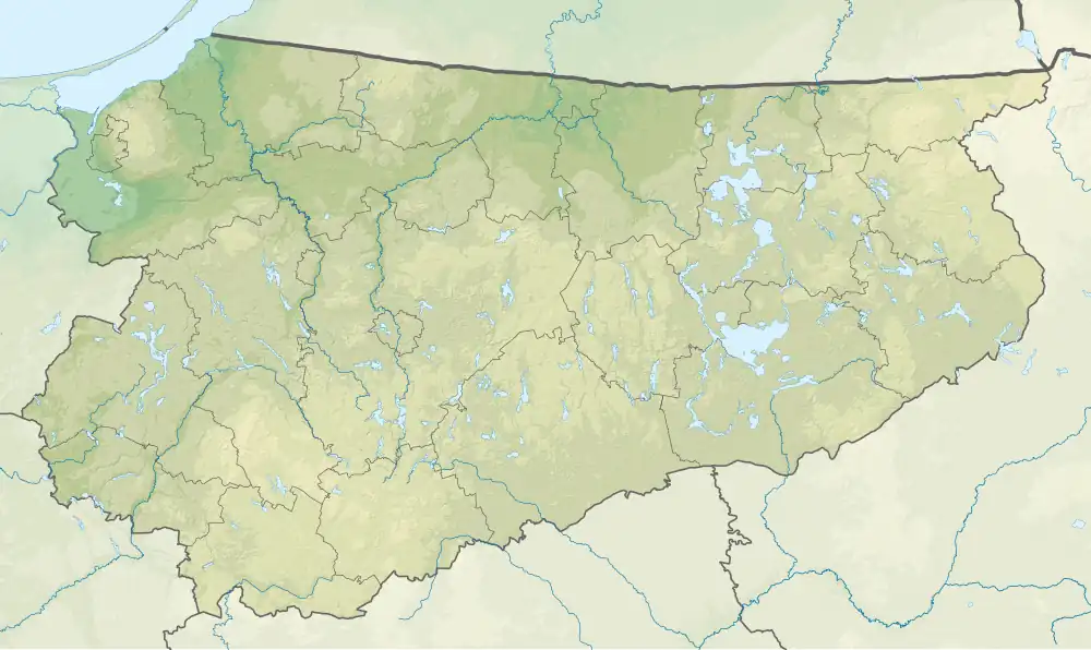 Mapa konturowa województwa warmińsko-mazurskiego, w centrum znajduje się owalna plamka nieco zaostrzona i wystająca na lewo w swoim dolnym rogu z opisem „Czarne Jezioro”